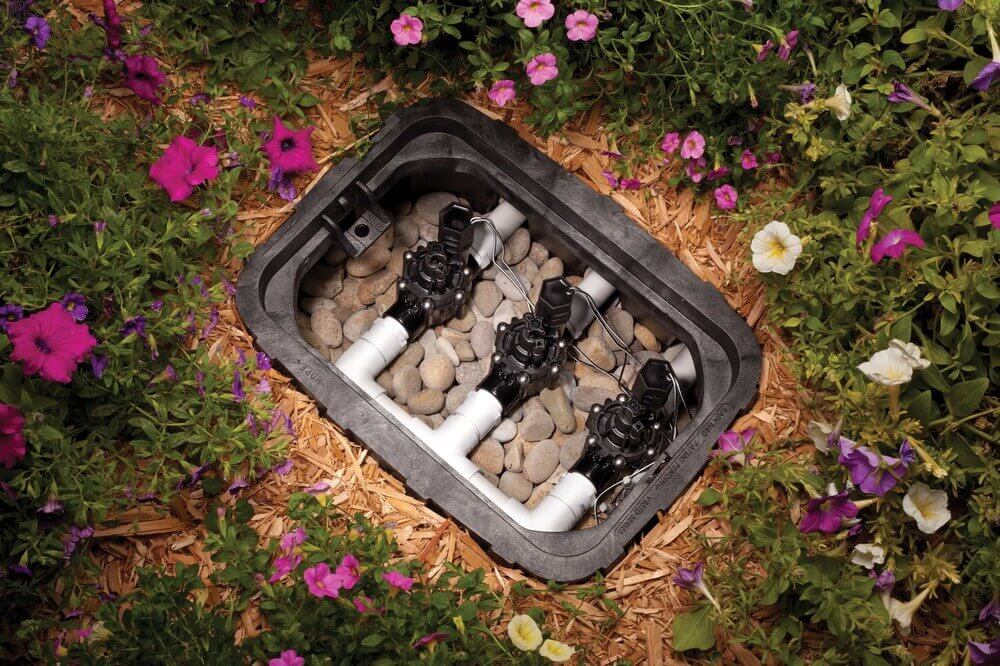 Irrigation valve box with solenoid valves and PVC pipes amid flowers in the Phoenix Metro Area.